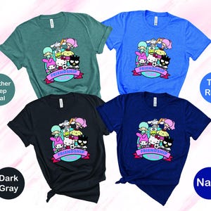May include: Four t-shirts in different colors with a graphic print of cartoon characters. The characters are wearing hats and holding a soccer ball. The text "Friendship Goals" is printed on the shirts. The colors of the shirts are heather deep teal, true royal, dark gray, and navy.