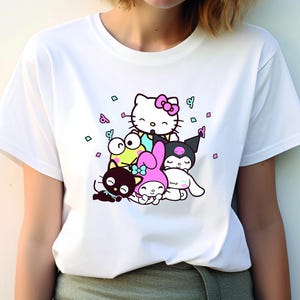 Pu&ograve; includere: Maglietta bianca con una stampa grafica di Hello Kitty e altri personaggi dei cartoni animati. I personaggi sono circondati da coriandoli.