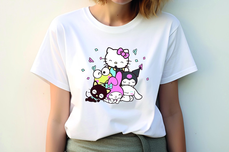 Pu&ograve; includere: Maglietta bianca con una stampa grafica di Hello Kitty e altri personaggi dei cartoni animati. I personaggi sono circondati da coriandoli.