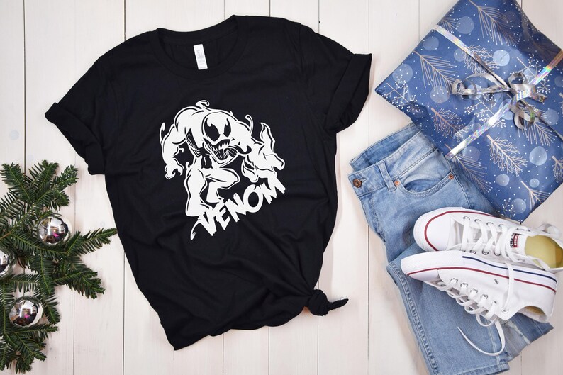 May include: Black t-shirt with a white graphic of Venom, a Marvel Comics character, with the word "Venom" printed below the image.