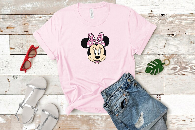 May include: A pink t-shirt with a black and white image of Minnie Mouse's face. Minnie Mouse is wearing a pink bow with white polka dots.
