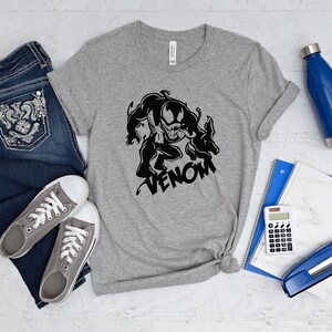 May include: A gray t-shirt with a black and white graphic of Venom, a Marvel Comics character. The graphic shows Venom in a menacing pose with the word "Venom" written below it.