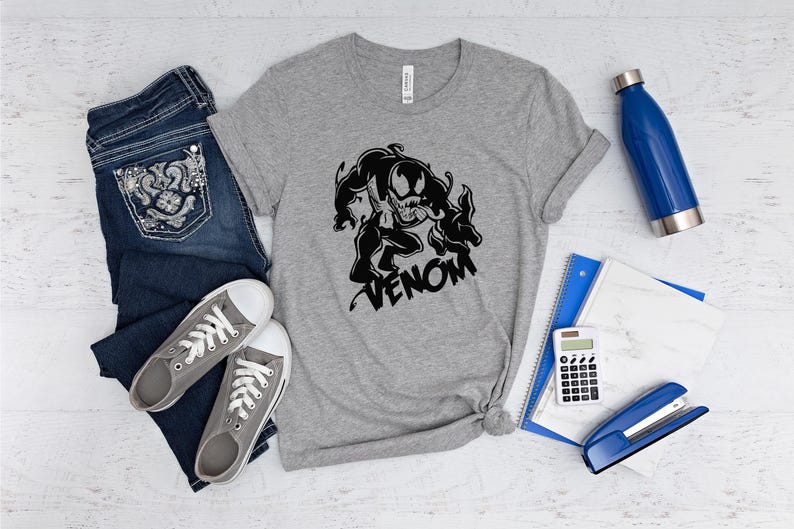 May include: A gray t-shirt with a black and white graphic of Venom, a Marvel Comics character. The graphic shows Venom in a menacing pose with the word "Venom" written below it.