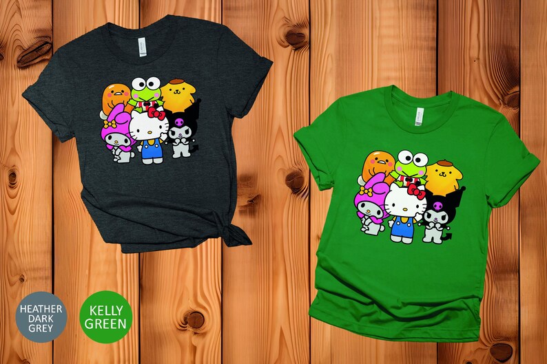May include: Two t-shirts featuring a graphic print of a group of cartoon characters. The characters include Hello Kitty, My Melody, Keroppi, Badtz-Maru, and a yellow chick. The shirt on the left is heather dark grey and the shirt on the right is kelly green.