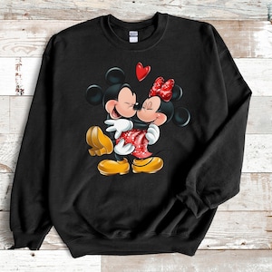 May include: Black sweatshirt with a graphic of Mickey Mouse and Minnie Mouse hugging with a red heart above them.