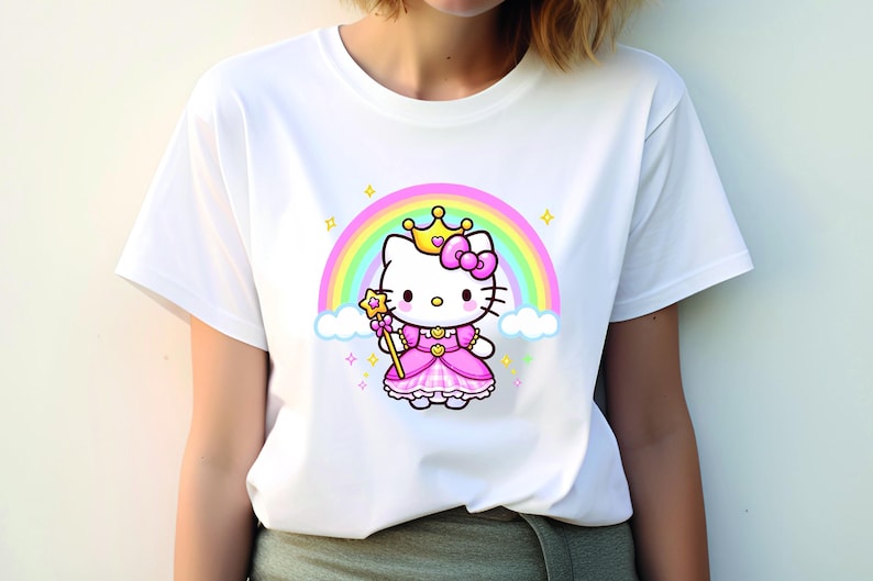 May include: White t-shirt featuring a cartoon princess cat with a crown, bow, and wand, set against a rainbow and clouds. The cat wears a pink dress. The design includes stars and sparkles.