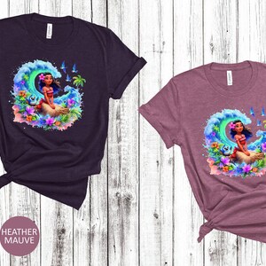 Peut inclure: Deux t-shirts avec un motif aquarelle d'un personnage de dessin anim&eacute; sur une vague. Le personnage a de longs cheveux bruns et porte une fleur derri&egrave;re l'oreille. Le motif comprend des couleurs bleues et vertes. Les t-shirts sont disponibles en marron chin&eacute; et mauve chin&eacute;.