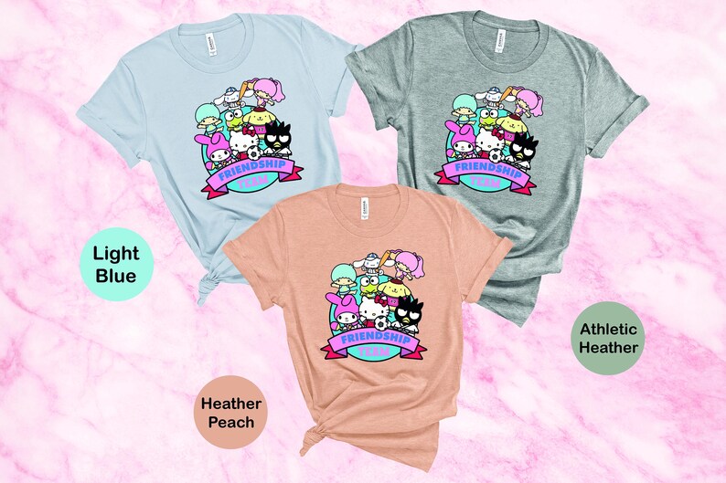 May include: Three t-shirts with a graphic print of cartoon characters. The t-shirts are in light blue, heather peach, and athletic heather colors. The graphic features a group of cartoon characters with the text "Friendship Goals".