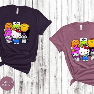 May include: Two t-shirts featuring a graphic print of cartoon characters. The left shirt is heather maroon and the right shirt is heather mauve. The graphic depicts a group of cartoon characters including Hello Kitty, Keroppi, My Melody, and Badtz-Maru.