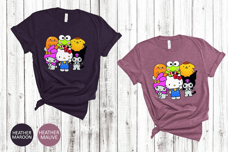 May include: Two t-shirts featuring a graphic print of cartoon characters. The left shirt is heather maroon and the right shirt is heather mauve. The graphic depicts a group of cartoon characters including Hello Kitty, Keroppi, My Melody, and Badtz-Maru.