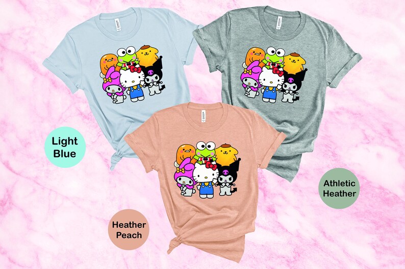 May include: Three t-shirts featuring a graphic print of cartoon characters. The t-shirts are in light blue, heather peach and athletic heather colours. The graphic features Hello Kitty and other cartoon characters.