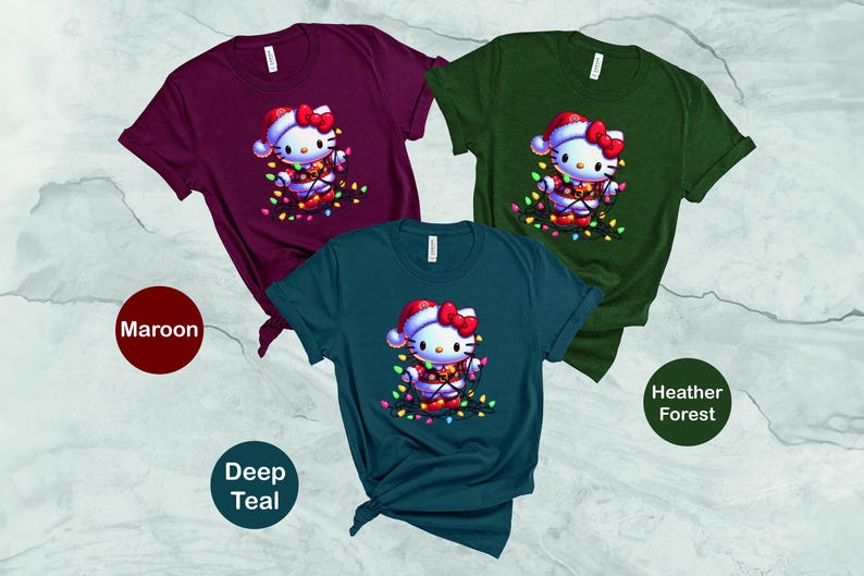 May include: Three t-shirts in maroon, deep teal, and heather forest green. Each shirt features a graphic of a cartoon cat wearing a Santa hat and wrapped in Christmas lights. The shirts are short-sleeved.