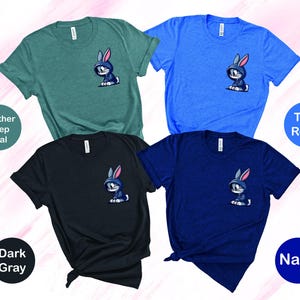 May include: Four t-shirts in different colors with a cartoon bunny rabbit graphic on the front. The colors are heather deep teal, dark gray, true royal, and navy.