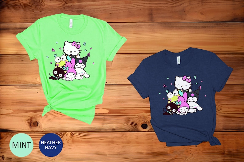 Pu&ograve; includere: Due t-shirt con una stampa grafica di Hello Kitty e i suoi amici. La maglietta a sinistra &egrave; di colore verde brillante e la maglietta a destra &egrave; di colore blu scuro.