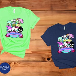 May include: Two t-shirts with a graphic print of cartoon characters. The green t-shirt has the text "Friendship Team" in a purple banner. The blue t-shirt has the same graphic and text.