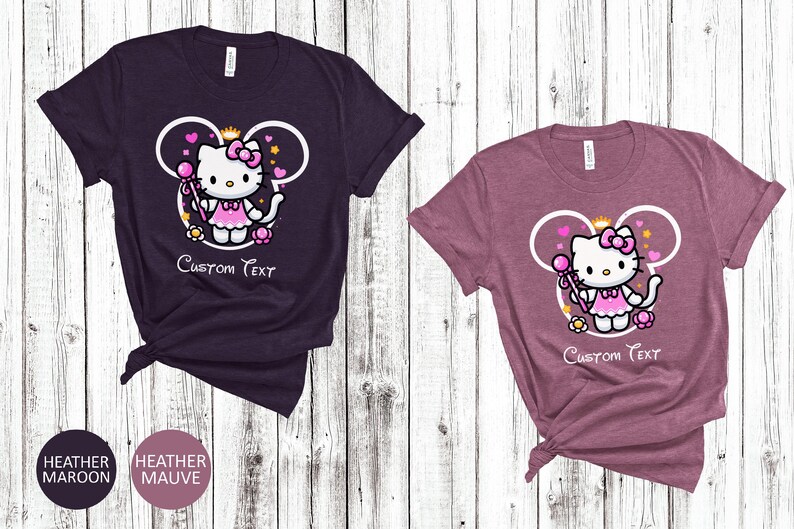 May include: Two t-shirts with a pink Hello Kitty character wearing a crown and holding a wand. The character is inside a white outline of Mickey Mouse ears. The text "Custom Text" is below the character. The t-shirts are heather maroon and heather mauve.