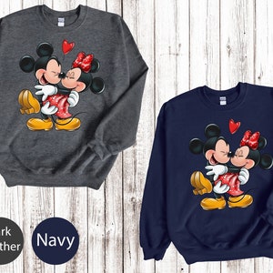 May include: A dark heather grey and a navy blue sweatshirt with a graphic of Mickey Mouse and Minnie Mouse kissing. The graphic is in red, yellow, and black.