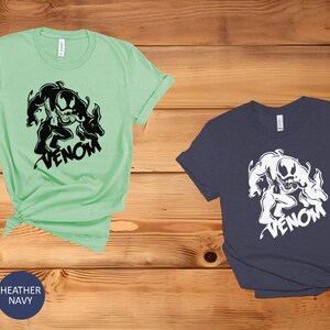 May include: Two t-shirts with a black and white graphic of Venom, a Marvel Comics character. The t-shirts are available in mint green and heather navy.