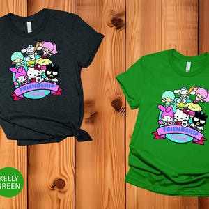 May include: Two t-shirts with a graphic print of cartoon characters. The t-shirt on the left is heather dark grey and the t-shirt on the right is kelly green. Both t-shirts feature the text "Friendship Team".
