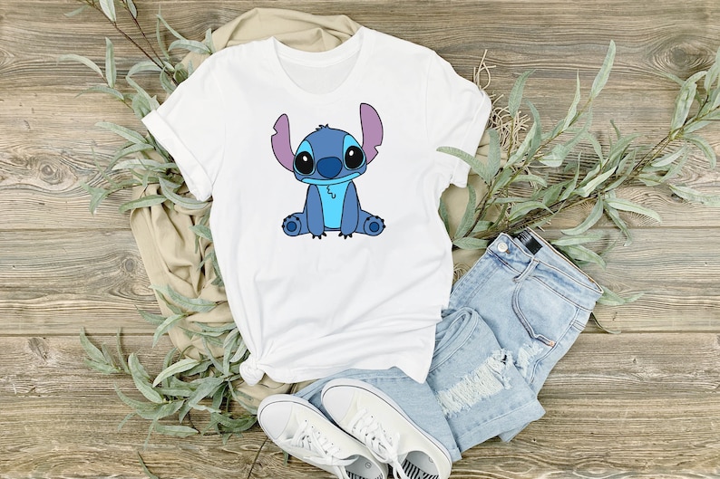 May include: White t-shirt with a blue cartoon Stitch character sitting on the front of the shirt.