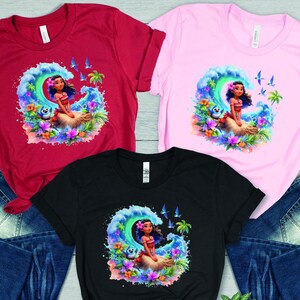 Peut inclure: Trois t-shirts avec une image de dessin anim&eacute; d'une fille aux longs cheveux noirs et une tenue bleue et verte chevauchant une vague. Les t-shirts sont rouge, rose et noir.