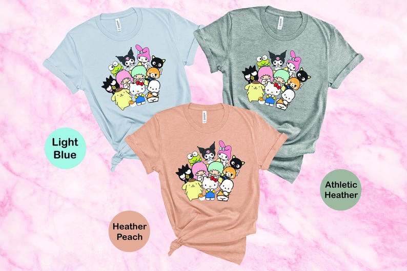 May include: Three t-shirts with a graphic print of a group of cartoon characters. The t-shirts are in light blue, heather peach, and athletic heather.