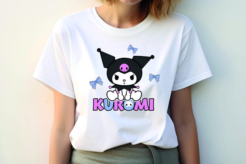 Puede incluir: Camiseta blanca con un dise&ntilde;o de personaje de dibujos animados. El personaje tiene una cabeza negra con una calavera rosa y un cuerpo blanco. La palabra "KUROMI" est&aacute; impresa en rosa y azul. Tambi&eacute;n se presentan lazos azul claro.