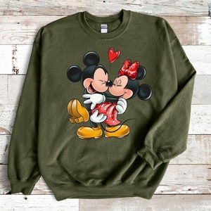May include: A green sweatshirt with a graphic print of Mickey Mouse and Minnie Mouse kissing. The graphic is in color and features a red heart above the couple.