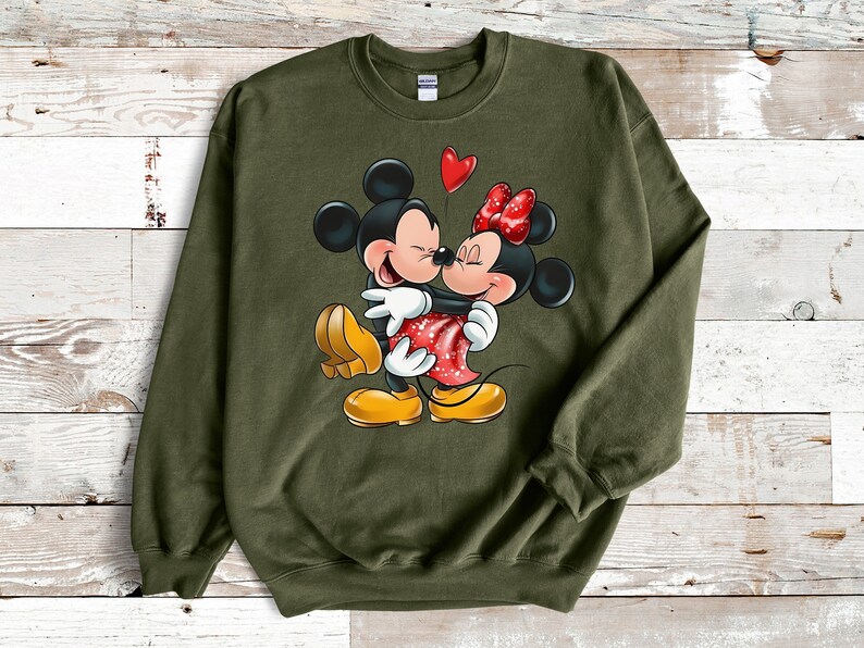 May include: A green sweatshirt with a graphic print of Mickey Mouse and Minnie Mouse kissing. The graphic is in color and features a red heart above the couple.