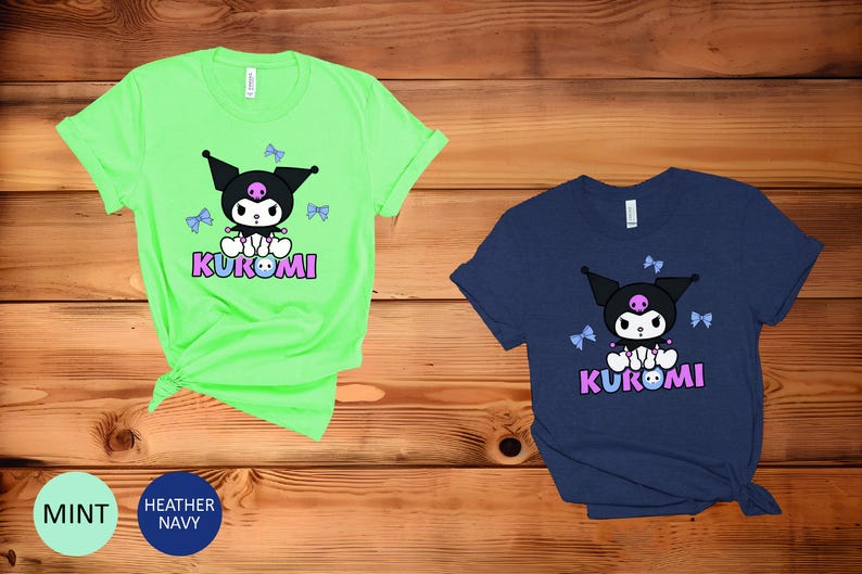 Puede incluir: Dos camisetas de manga corta, una verde menta y otra azul marino, con un personaje de dibujos animados con orejas negras, una calavera rosa y la palabra "KUROMI" en rosa y azul. El personaje est&aacute; rodeado de lazos azules.
