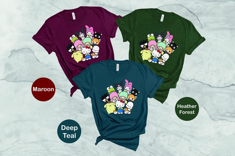May include: Three t-shirts with a graphic print of cartoon characters. The t-shirts are in maroon, deep teal, and heather forest colors. The graphic features a group of cartoon characters with a pink, green, and blue color scheme.