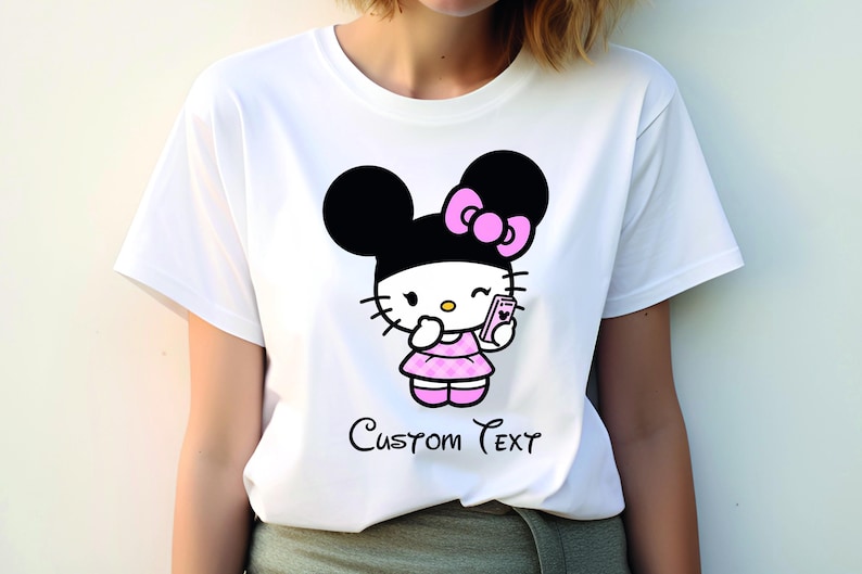 Pu&ograve; includere: T-shirt bianca con un personaggio dei cartoni animati con orecchie nere, un fiocco rosa e un vestito rosa, che tiene in mano un telefono. Il testo "Custom Text" &egrave; scritto in corsivo sotto.