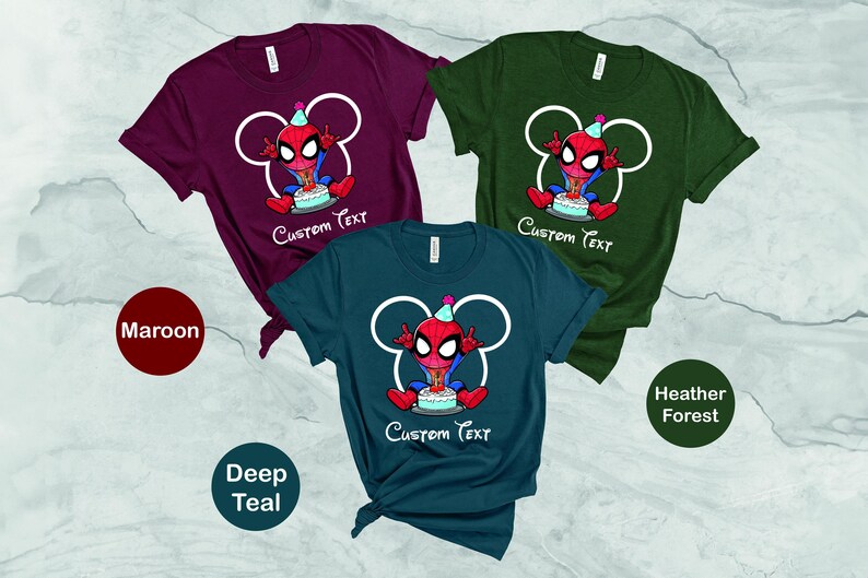 May include: Three short-sleeved t-shirts in maroon, deep teal, and heather forest green. Each shirt features a cartoon Spider-Man character with a birthday cake and the text "Custom Text" in white. The Spider-Man design is set within a white Mickey Mouse-shaped outline.