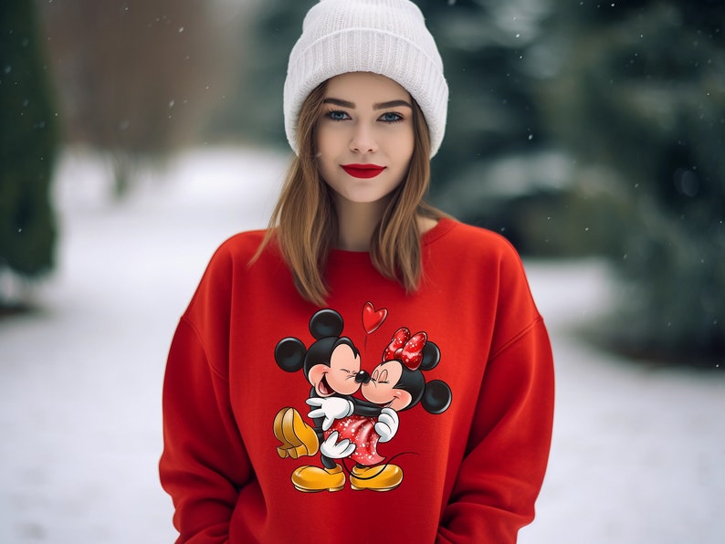 May include: A red sweatshirt with a graphic print of Mickey Mouse and Minnie Mouse kissing. The sweatshirt has a crew neck and long sleeves.