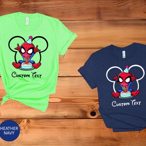 May include: Two short-sleeved t-shirts, one mint green and one navy blue, with a cartoon Spider-Man design and a birthday cake. The design includes a Mickey Mouse head outline and the text "Custom Text".