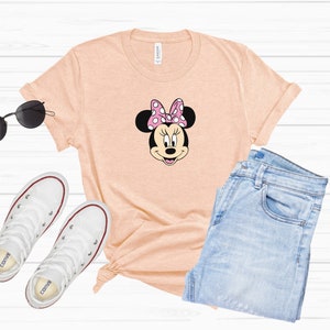 May include: A peach-colored t-shirt with a black and white cartoon image of Minnie Mouse wearing a pink bow with white polka dots.