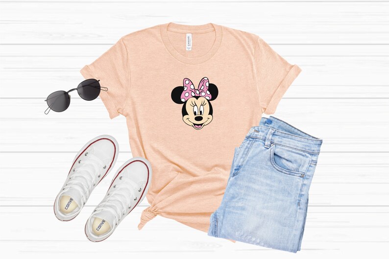 May include: A peach-colored t-shirt with a black and white cartoon image of Minnie Mouse wearing a pink bow with white polka dots.