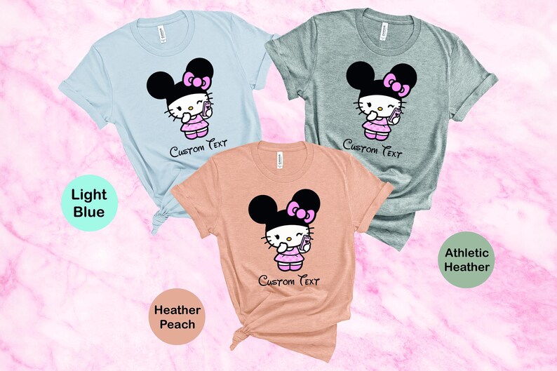 Pu&ograve; includere: Tre magliette a maniche corte in azzurro, grigio atletico e pesca melange. Ogni maglietta presenta un personaggio dei cartoni animati con una testa nera a forma di orecchio di topo, un fiocco rosa e un vestito rosa, che tiene in mano un telefono. Il testo "Custom Text" &egrave; sotto.