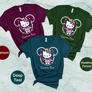 May include: Three t-shirts with a cartoon image of a princess wearing a crown and holding a wand. The t-shirts are maroon, deep teal, and heather forest green. The text "Custom Text" is printed on each shirt.
