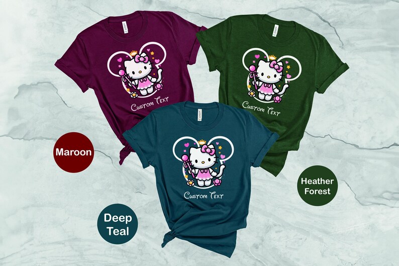 May include: Three t-shirts with a cartoon image of a princess wearing a crown and holding a wand. The t-shirts are maroon, deep teal, and heather forest green. The text "Custom Text" is printed on each shirt.