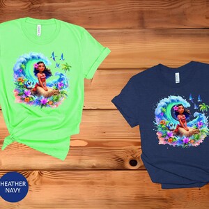Peut inclure: Deux t-shirts avec une illustration color&eacute;e d'un personnage de dessin anim&eacute; sur une vague. Le personnage porte un collier de fleurs et a de longs cheveux bruns. Les t-shirts sont disponibles en vert menthe et bleu marine chin&eacute;.