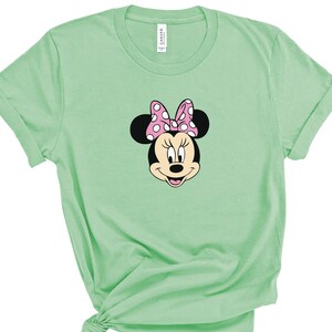 May include: A light green t-shirt with a cartoon image of Minnie Mouse wearing a pink polka dot bow.