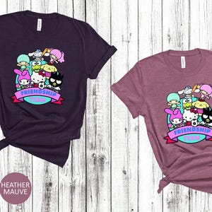 May include: Two t-shirts with a graphic print of cartoon characters. The graphic features a group of cartoon characters with the text "Friendship Team". The t-shirts are available in heather maroon and heather mauve.