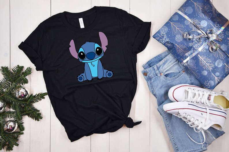 May include: Black t-shirt with a blue Stitch character from Lilo & Stitch. The character is sitting with its arms crossed and has a light blue body and purple ears.
