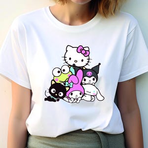 K&ouml;nnte beinhalten: Wei&szlig;es T-Shirt mit einem Grafikdruck von Hello Kitty und ihren Freunden. Die Figuren sind &uuml;bereinander gestapelt, mit Hello Kitty oben. Die Figuren sind alle in Schwarzwei&szlig;, au&szlig;er Hello Kittys rosa Schleife.