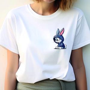 May include: White t-shirt with a cartoon image of a blue rabbit wearing a blue hoodie. The rabbit has pink ears and is sitting down.