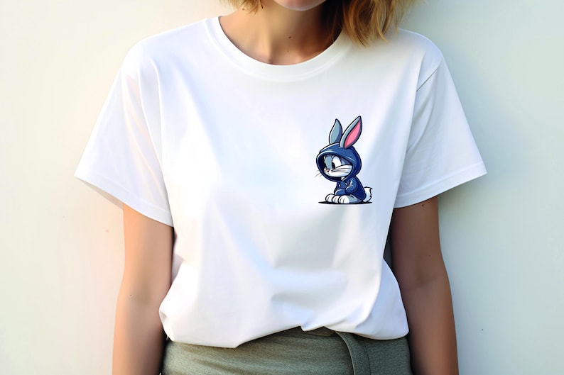 May include: White t-shirt with a cartoon image of a blue rabbit wearing a blue hoodie. The rabbit has pink ears and is sitting down.