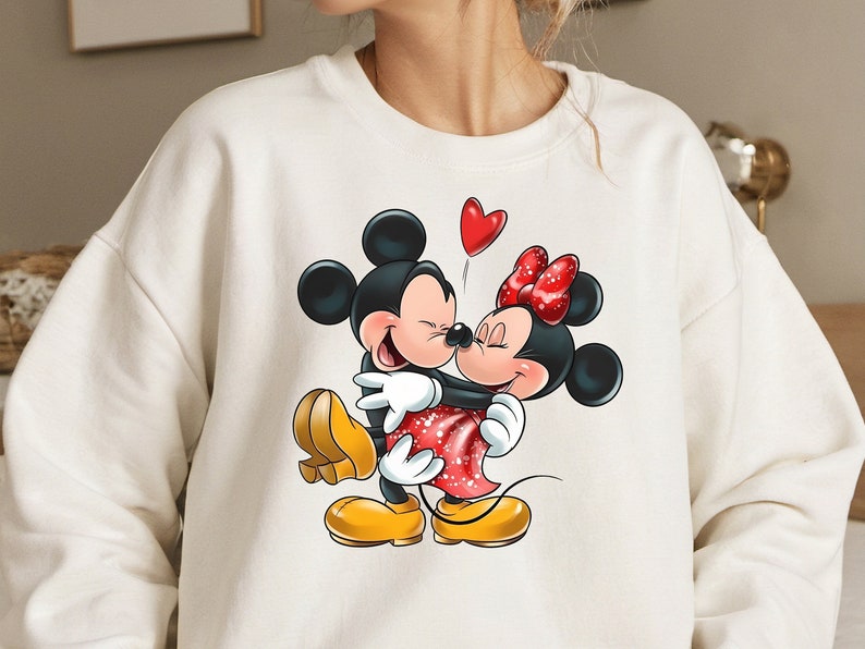May include: White sweatshirt with a graphic print of Mickey Mouse and Minnie Mouse hugging. The graphic is in red, black, and white. A red heart is above the characters.