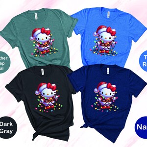 May include: Four short-sleeved t-shirts in teal, blue, dark gray, and navy. Each shirt features a cartoon character wearing a Santa hat and wrapped in Christmas lights. The shirts are labeled "Heather Deep Teal", "True Royal", "Dark Gray", and "Navy".