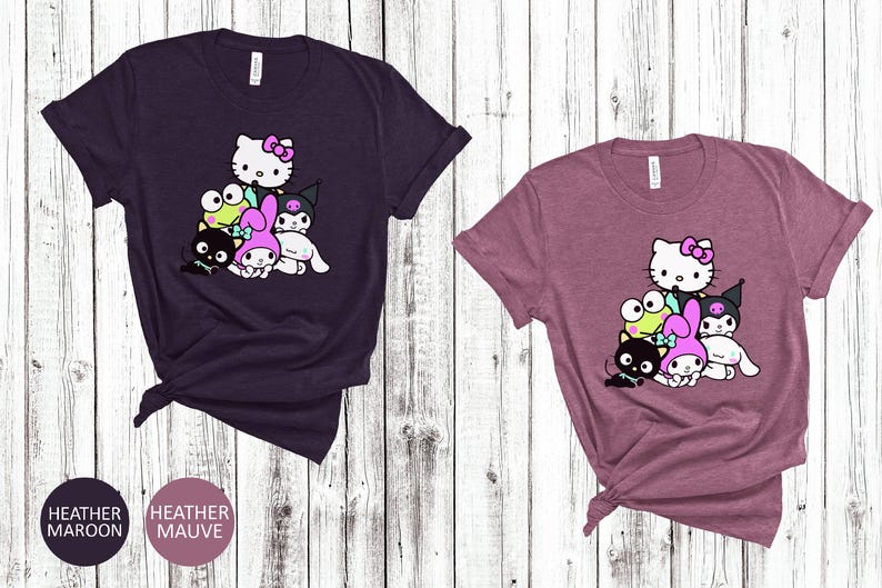 K&ouml;nnte beinhalten: Zwei T-Shirts mit einem Grafikdruck einer Gruppe von Comicfiguren. Die Figuren sind Hello Kitty, My Melody, Kuromi und ein Frosch. Die T-Shirts sind in den Farben Heather Maroon und Heather Mauve erh&auml;ltlich.